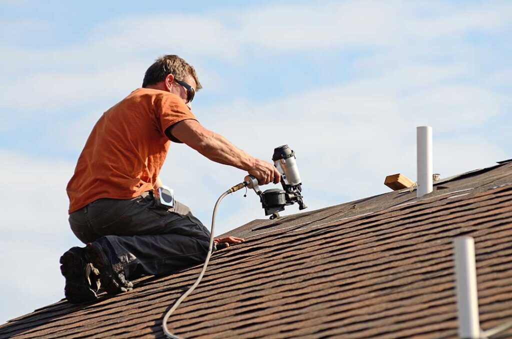 Rainwater flows from a shingled roof into clean gutters and downspouts beside a residential home.