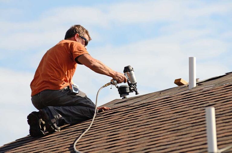 Rainwater flows from a shingled roof into clean gutters and downspouts beside a residential home.