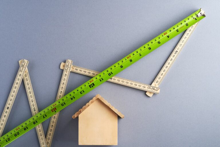 A homeowner measures roof pitch with a level and tape measure beside exposed attic rafters.